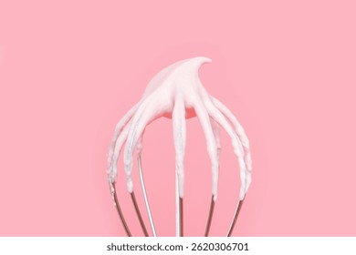 Whisk with whipped cream from proteins close-up on pink background.