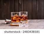 Whiskey, bourbon or cognac on glass with ice cube on a rustic wooden background with copy space
