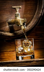 Whiskey Or Brandy Is Poured Into A Glass From Oak Barrel