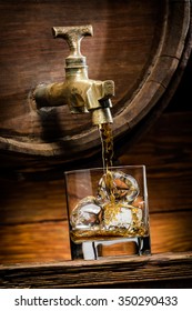 Whiskey Or Brandy Is Poured Into A Glass From Oak Barrel