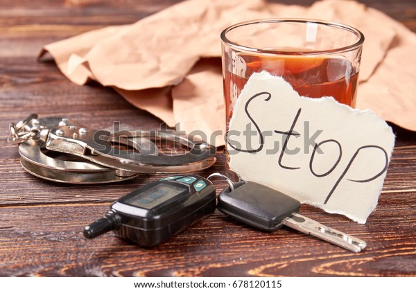 Whiskey with car keys and handcuffs. Message\
stop, glass of alcohol, metal handcuffs on wooden background. Stop\
drink and be\
responsible.