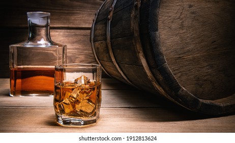 Whiskey Drinks. Whiskey In A Glass With Ice Cubes On A Wooden Table Next To A Barrel Of Whiskey And A Bottle Of Whiskey On A Wooden Background.