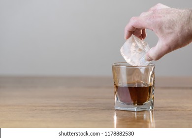 Whiskey In An Elegant Glass On The Rocks With A Large Ice Cube On A Rustic Wood Table.