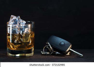 Whiskey glass with ice and car keys on a rustic wooden table, dark background with copy space, concept alcohol and driving