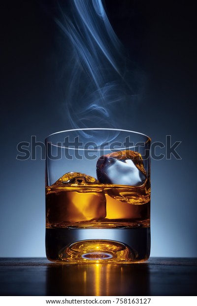 Whiskey glass and ice on a wooden bar table. Smoke and\
whiskey. 