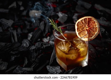 Whiskey with ice, dried orange slice, and rosemary. Whiskey with rosemary and beautiful swirls of smoke on a background of burning charcoal. - Powered by Shutterstock