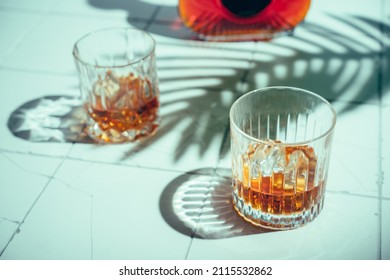 Whiskey With Ice In Glasses And Bottle, White Background With Hard Light, Shadows And Sun Glare, Copy Space
