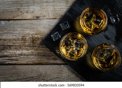 Whiskey with ice in glasses, rustic wood background, copy space