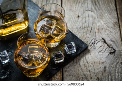 Whiskey with ice in glasses, rustic wood background, copy space