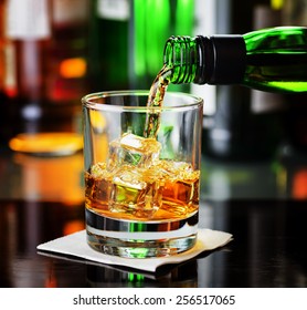 Whiskey Pouring From A Bottle Into A Glass In A Bar. Scotch And Irish Single Malt Or Blended Whiskey.