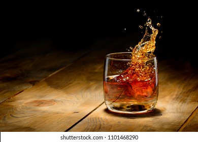 Whiskey splash in glass on a wooden table.