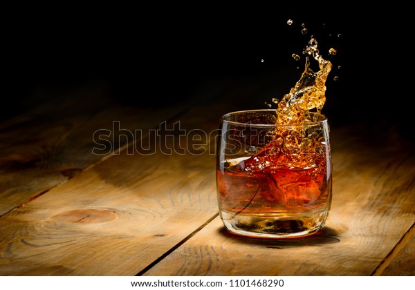 Whiskey splash in\
glass on a wooden\
table.