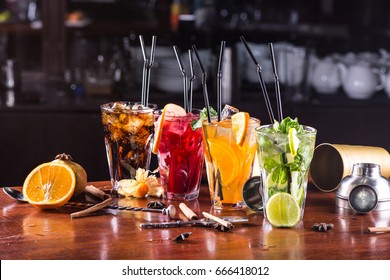 Whiskey-cola cocktail, mojito-cocktail, orange cocktail, strawberry cocktail in glass glasses with straws. Bar accessories: shaker, spoon, spices on a wooden stand - Shutterstock ID 666418012
