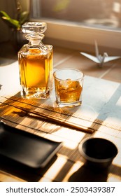 Whisky bottle with tumbler filled with Whisky and icecubes in japanese Atmosphere with Sushiplate and chopsticks 