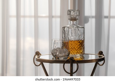 Whisky glass decanter hall-full with whisky liquor and two glasses with ice rocks on glass table in cozy hotel interior