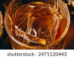 Whisky on the rocks. Glass of aged bourbon, whiskey, cognac, scotch filled with ice cube, close-up macro photo. Alcohol, hard drink concept