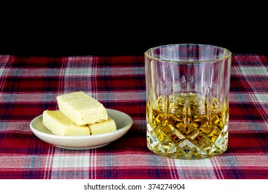 Whisky And Shortbread On Tartan Table Cloth Against Black Background