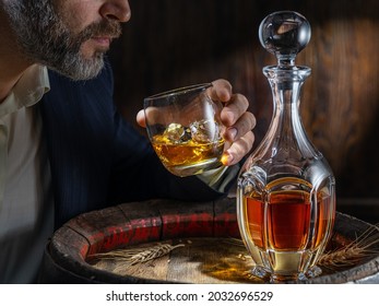 Whisky tasting. Man sits in front of a barrel with a decanter and a glass of whiskey.