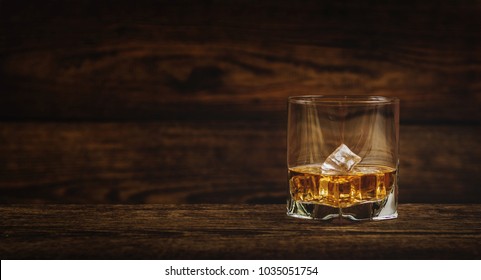 Whisky or whiskey or bourbon with ice on wood background