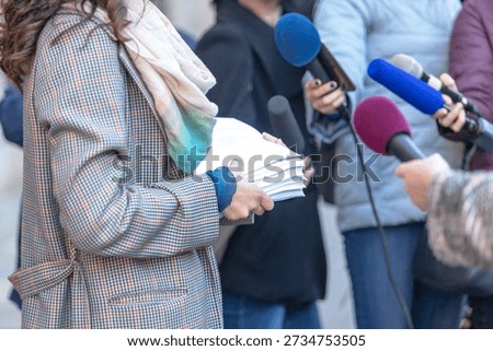 Whistleblower holding documents giving statement at press conference, speaking to journalists with microphones, concept of corruption exposure, public interest, media coverage, political communication and journalism