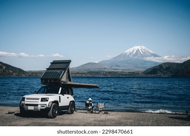 White 4x4 overland car with rooftop tent and awning at the beach and a lake with a view of Mountain Fuji, Japan. 