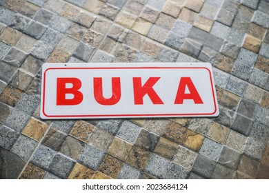 A white acrylic board with the words Open (Buka) in red in Indonesian is placed on a stone-patterned ceramic - Shutterstock ID 2023684124
