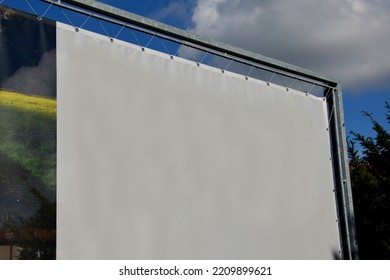 white advertising tarpaulin installed by a cable into the metal galvanized frame and shackled holes. Movable advertising solution, easily replaceable content for medium-term outdoor use company - Shutterstock ID 2209899621