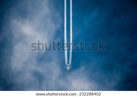 White airliner transports passengers while it pulling white contrails in dark blue cloudy sky