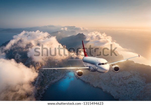 夏の夕暮れに白い飛行機が山や低い雲の上を飛んでいる 美しい旅客機の風景 雲 海 日差し 旅行 商用機 航空機の空中図 の写真素材 今すぐ編集