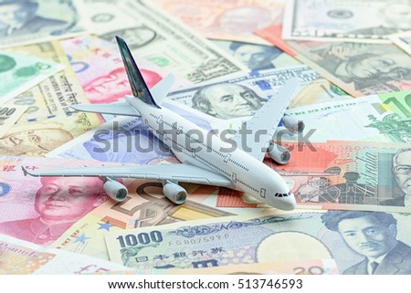 White airplane lands on a pile of banknotes from the most dominant countries around the world i.e. US dollar, Chinese CNY yuan, Japanese yen, Indian rupee, Australian dollar, Euro. Aviation concept.