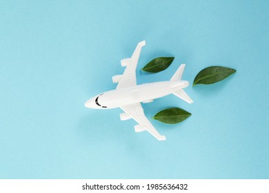 White Airplane Model Emitting Fresh Green Leaves On Blue Background. Clean And Green Energy, Biofuel For Aviation Industry Concept.