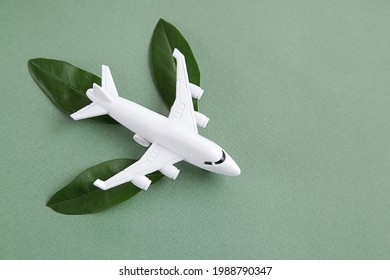 White Airplane Model Emitting Fresh Green Leaves On Green Background. Sustainable Travel, Clean And Green Energy, Biofuel For Aviation Industry Concept. Copy Space