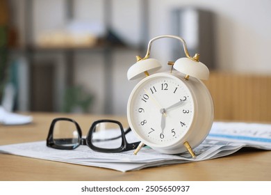 White alarm clock with eyeglasses on desk in office, closeup