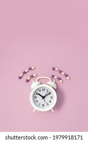 White Alarm Clock Surrounded By Multi-colored Pills On Pink Background. Time To Take Vitamins Concept. Vertical Banner. Copy Space.