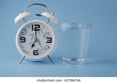 White Alarm Clock And Water Glass On Pastel Background.