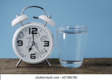 White Alarm Clock And Water Glass On Pastel Background.