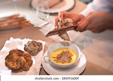 White Alba truffle sliced by the waiter's hands on fontina fondue in an elegant white ceramic cup with two handles on the saucer next to two large truffles