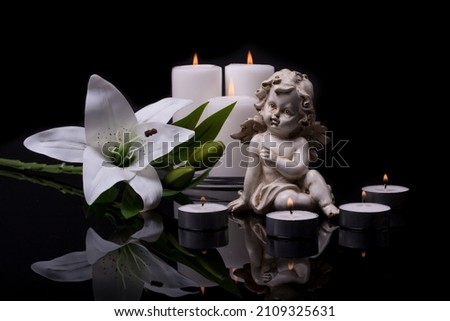 White angel with burning candles and white lily flower on a black background. 