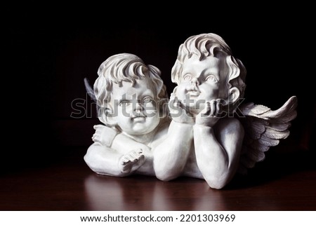 White angels on a dark background. The angels rest their face on their hands and dreamily look into the distance. High quality photo