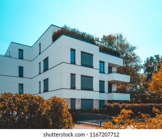 White Apartment Complex With Small Park And Bushes In The Foreground