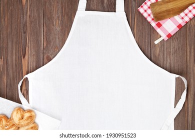 White Apron Template On Brown Wooden Table With Cookies. Kitchen, Cooking Clothing Mock Up.