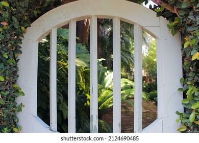 White arched gate doorway entrance to garden path enclosed by a plant-covered wall.