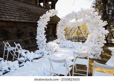 A white archway with white flowers and white chairs. The chairs are arranged in a semi circle around the archway - Powered by Shutterstock