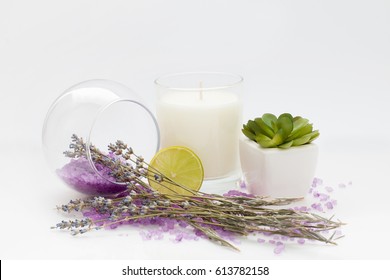 White Aroma Candle In A Glass With Purple Bath Salt And Dry Lavender Twigs And Lime Slice On A White Background