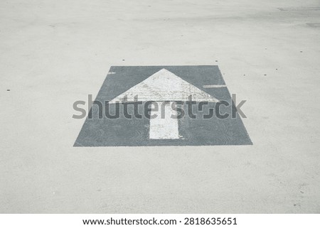 A white arrow with a black background on top of a sunny parking garage in asphalt
