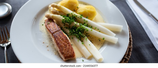 White asparagus with hollandaise sauce and fried salmon on a white plate in a restaautant. Close-up. Seasonal gastronomy presented in a modern way. Top view. 