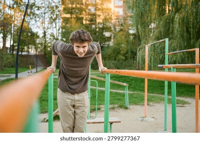 White athletic man performing parallel dips with controlled posture, outdoor calisthenics park setting with orangegreen equipment, intense focused gaze, apartment blocks and trees in background,