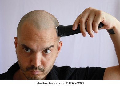 white average bald man shaving his head with an electric razor