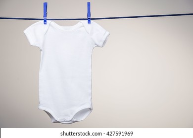White baby bodysuit hanging on a clothesline on grey background. Mock up