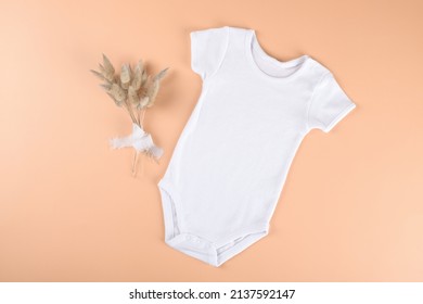 White Baby Bodysuit Mockup On Neutral Beige Pastel Color Background With Dry Plants, Modern Boho Decoration. Empty Place For Text Or Logo On Apparel. Design Bodysuit Template